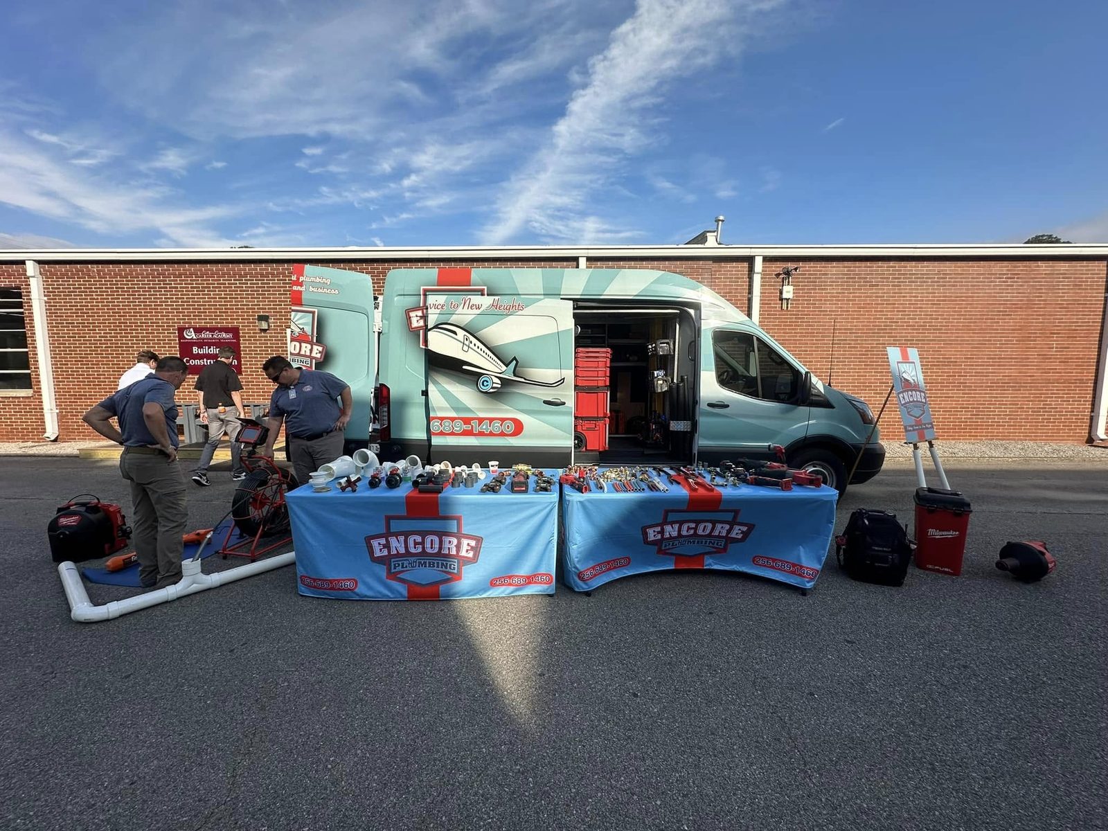 Encore Plumbing van and display tables set up outside a career academy building