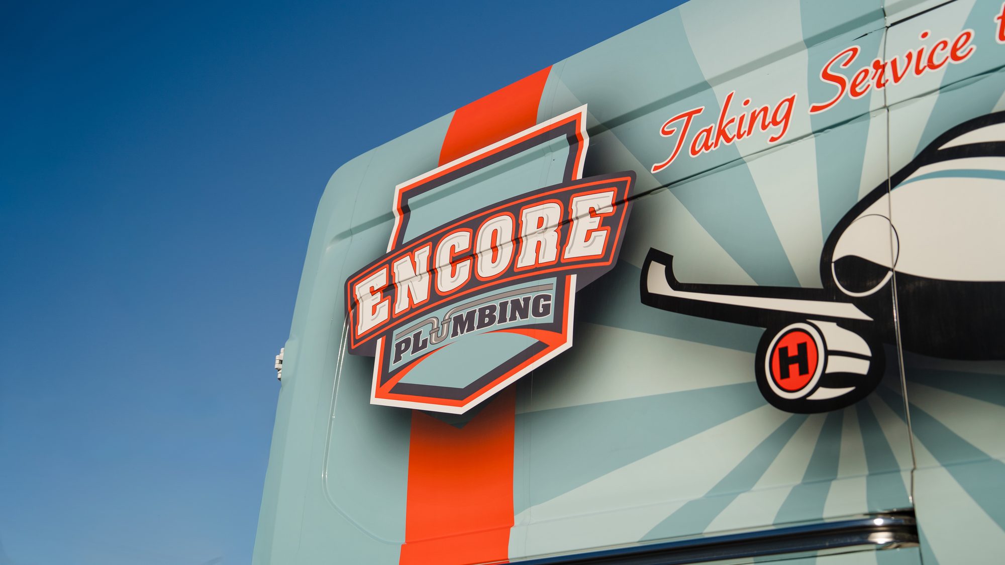 Close-up of the Encore Plumbing badge logo and Taking Service to New Heights lettering on the van