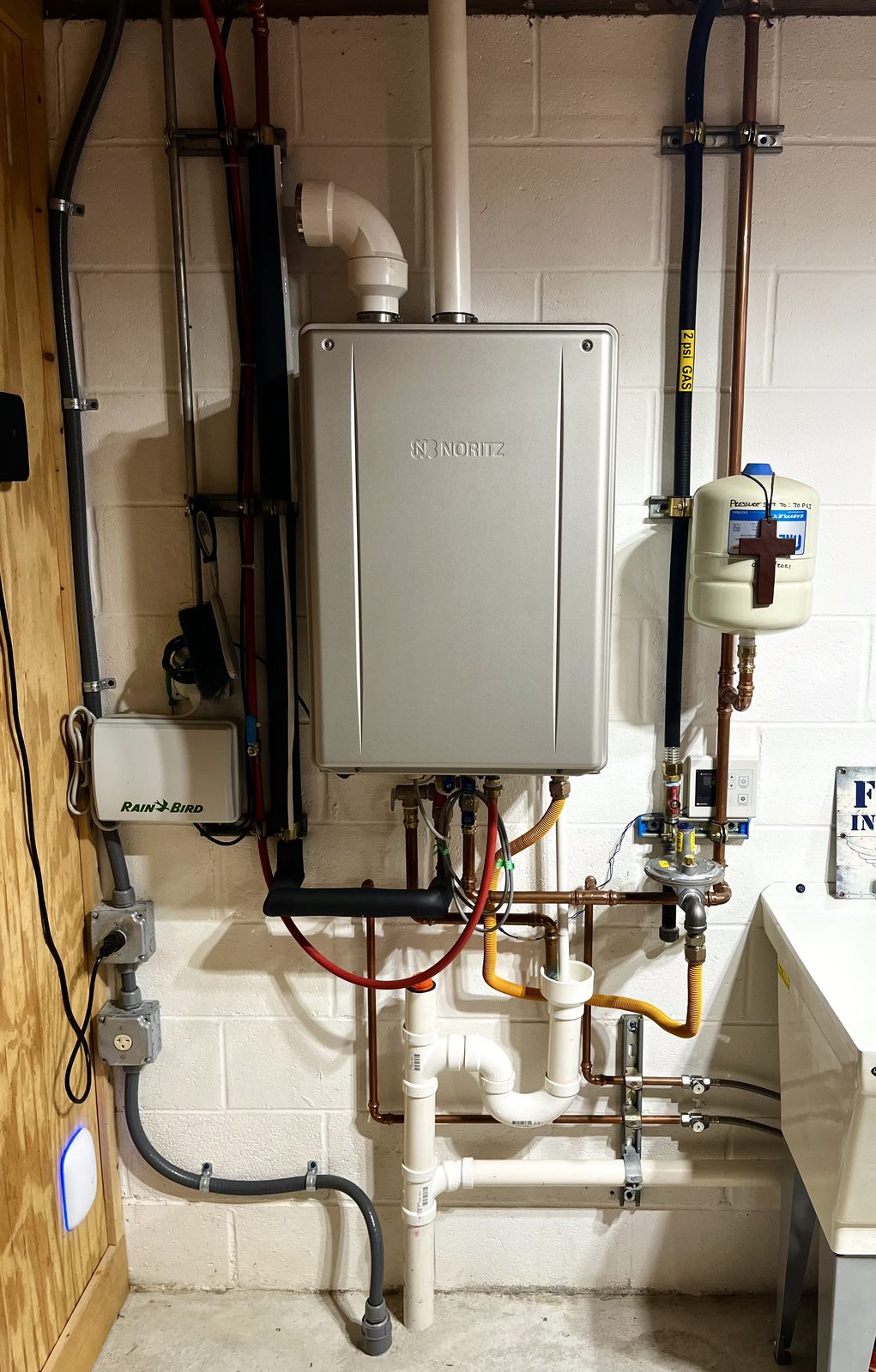 Noritz tankless water heater on a basement block wall with an expansion tank, gas line and condensate drain