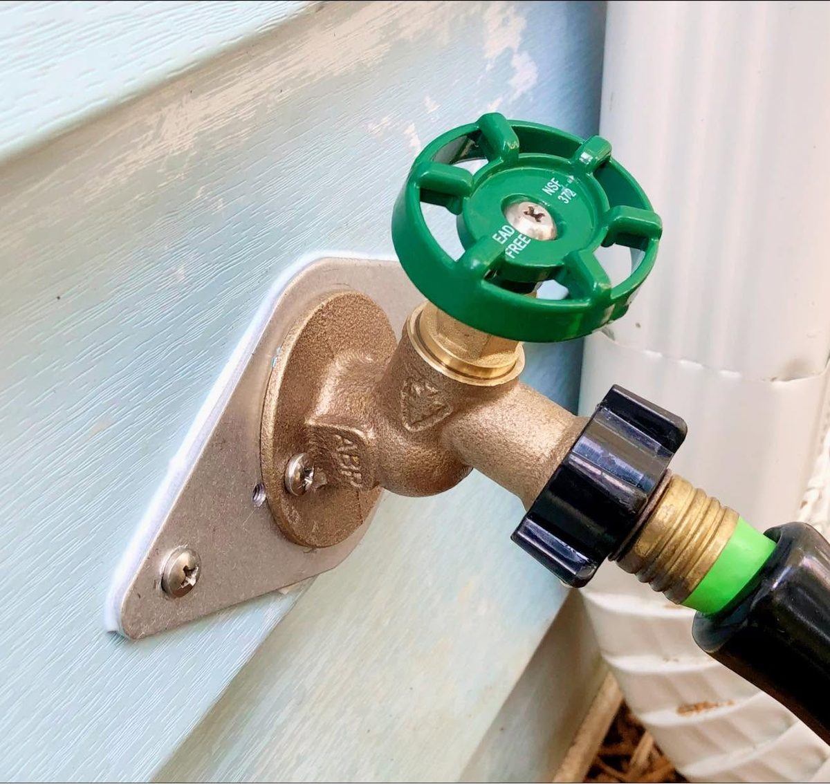 New brass frost-free hose bib with a green handle installed on light blue siding