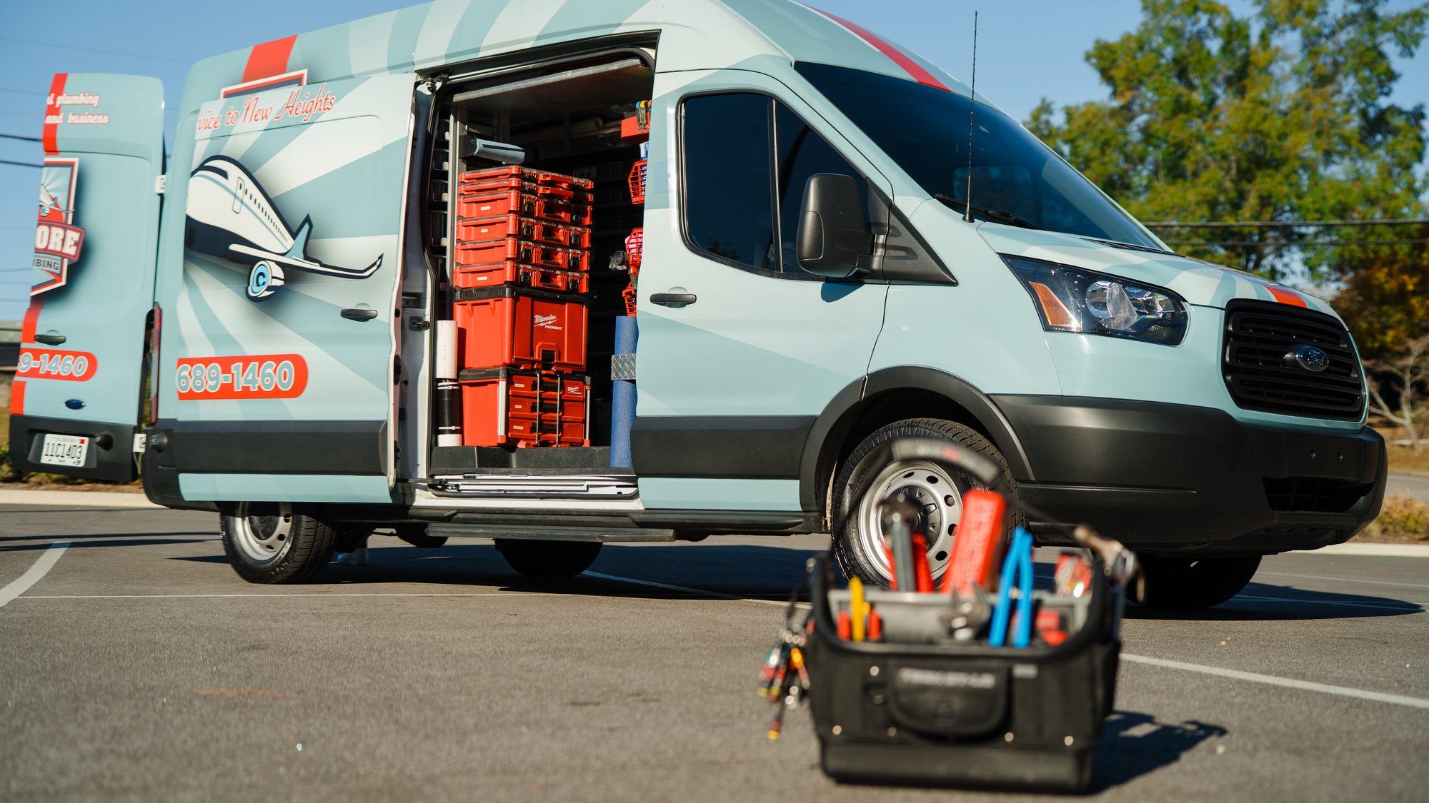 Encore Plumbing van with the side door open showing stacked red tool cases and shelving
