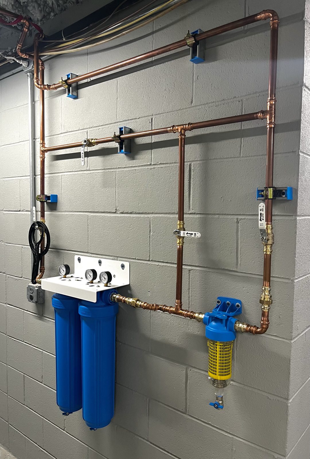 Twin blue whole-home filter housings with pressure gauges and a spin-down sediment filter on new copper piping